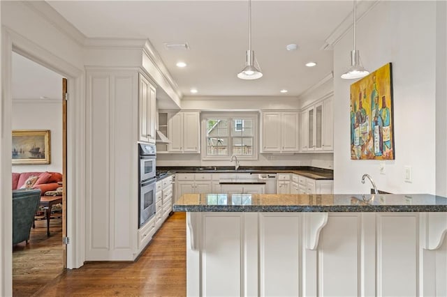 kitchen featuring a peninsula, wood finished floors, decorative light fixtures, and white cabinets