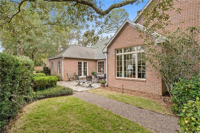 back of house featuring french doors, brick siding, a patio, and a lawn