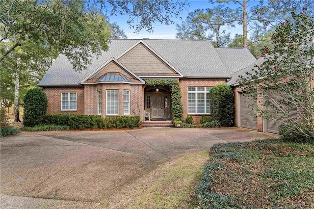 view of front of home featuring a shingled roof, concrete driveway, and brick siding