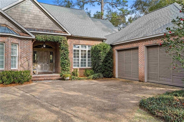 exterior space featuring driveway, roof with shingles, and brick siding