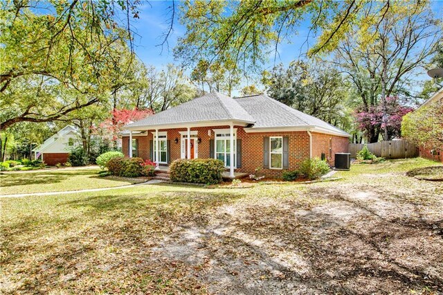 view of front facade featuring a front yard, fence, central AC unit, roof with shingles, and brick siding
