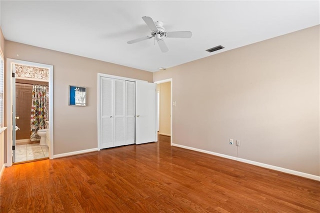 unfurnished bedroom with baseboards, visible vents, wood finished floors, ensuite bathroom, and a closet