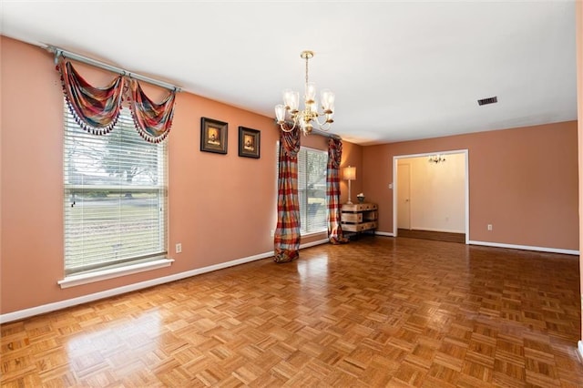 unfurnished room with baseboards, visible vents, and a notable chandelier