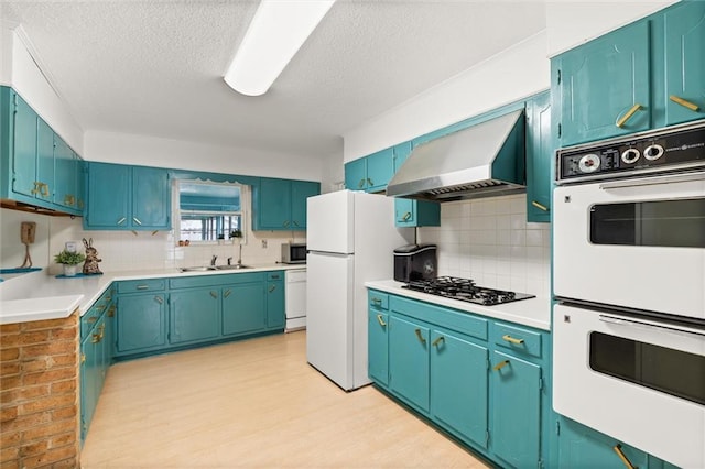 kitchen featuring white appliances, a sink, light countertops, range hood, and tasteful backsplash