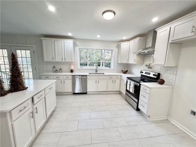 kitchen featuring wall chimney range hood, sink, tasteful backsplash, white cabinetry, and stainless steel appliances