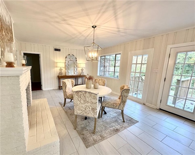 dining room featuring a brick fireplace, wooden walls, and an inviting chandelier