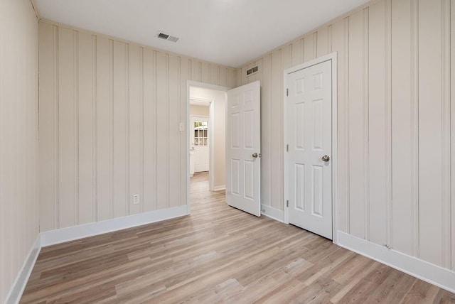 empty room with light wood-style floors, visible vents, and baseboards