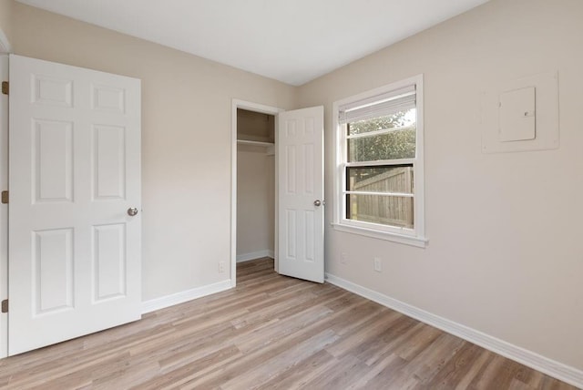 unfurnished bedroom featuring light wood-style flooring, electric panel, baseboards, and a closet