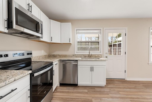 kitchen with light stone counters, appliances with stainless steel finishes, a sink, and white cabinetry