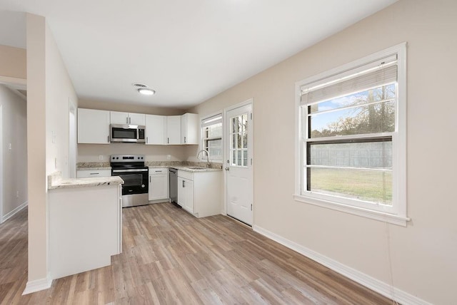 kitchen featuring baseboards, white cabinets, light wood-style flooring, stainless steel appliances, and a sink