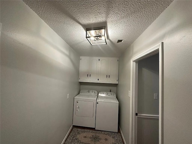 clothes washing area featuring washing machine and clothes dryer, a textured ceiling, baseboards, and cabinet space