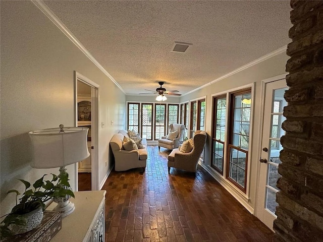 living room with a textured ceiling, visible vents, crown molding, a ceiling fan, and baseboards