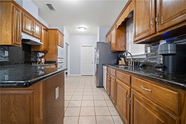 kitchen with light tile patterned floors, white appliances, dark stone countertops, and sink