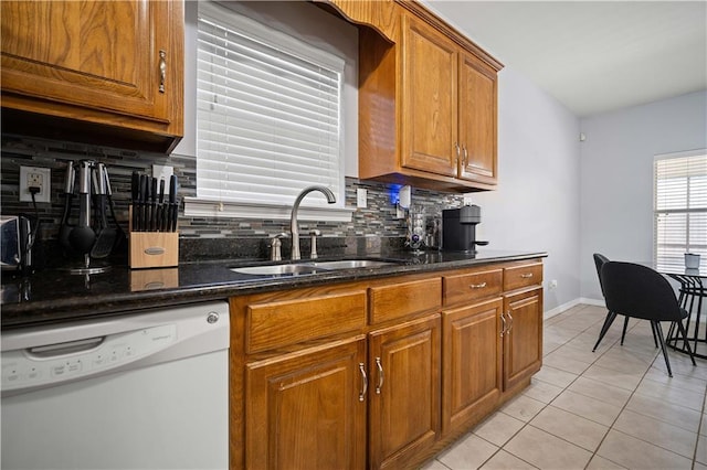 kitchen featuring dark stone counters, white dishwasher, sink, tasteful backsplash, and light tile patterned flooring