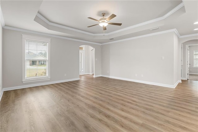 empty room with crown molding, a raised ceiling, ceiling fan, and light wood-type flooring