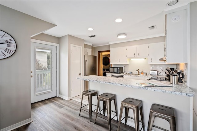 kitchen featuring a peninsula, stacked washer / drying machine, black microwave, white cabinets, and baseboards