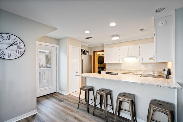 kitchen featuring stacked washer / drying machine, a peninsula, stove, white cabinetry, and light wood-type flooring