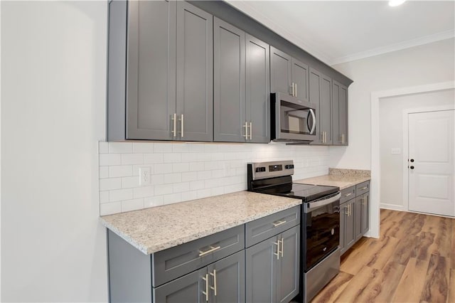 kitchen with light stone countertops, light wood-type flooring, gray cabinets, appliances with stainless steel finishes, and ornamental molding