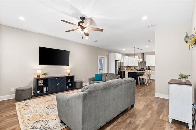 living room with ceiling fan, wood finished floors, visible vents, and baseboards