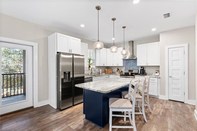 kitchen with stainless steel appliances, visible vents, a center island, wall chimney exhaust hood, and decorative light fixtures