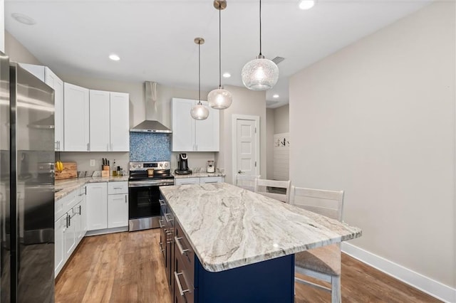 kitchen with stainless steel appliances, a kitchen island, white cabinets, wall chimney range hood, and decorative light fixtures