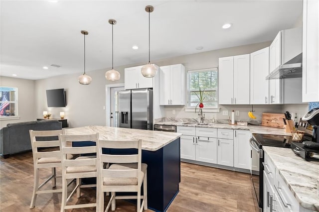 kitchen featuring a center island, appliances with stainless steel finishes, white cabinets, a sink, and wall chimney exhaust hood