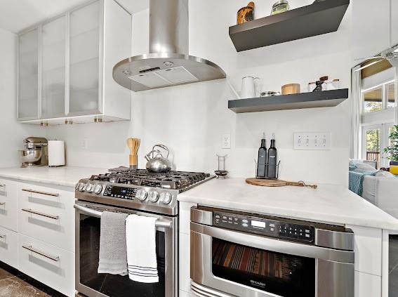 kitchen with white cabinets, appliances with stainless steel finishes, and wall chimney range hood