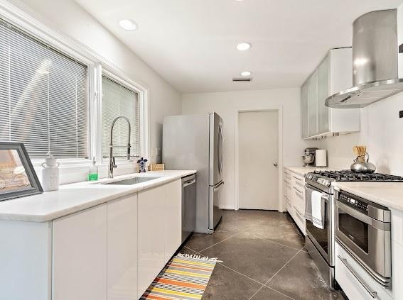 kitchen featuring wall chimney range hood, stainless steel appliances, sink, white cabinetry, and dark tile floors