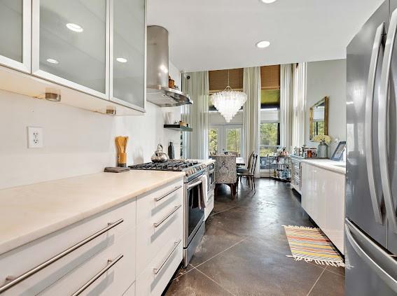 kitchen featuring white cabinets, wall chimney exhaust hood, appliances with stainless steel finishes, and an inviting chandelier