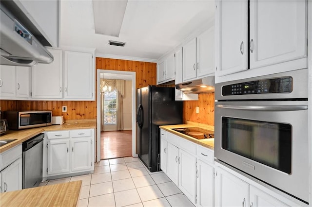 kitchen featuring light tile patterned flooring, wood walls, white cabinetry, crown molding, and black appliances