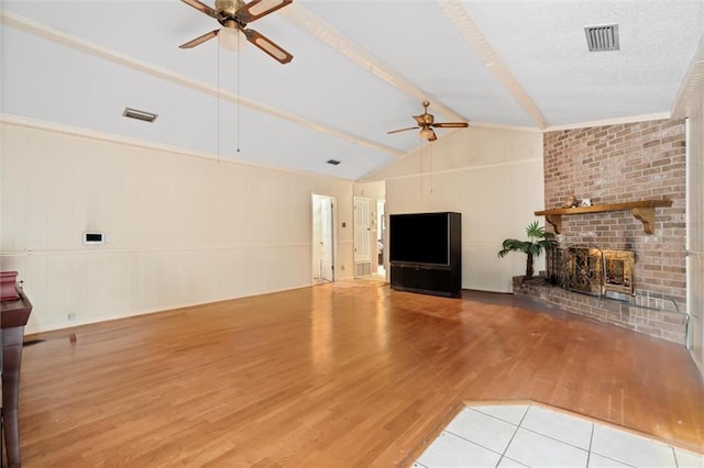 unfurnished living room featuring vaulted ceiling with beams, ceiling fan, light hardwood / wood-style floors, a brick fireplace, and a textured ceiling