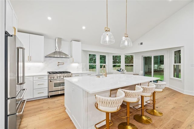 kitchen featuring white cabinets, wall chimney range hood, decorative backsplash, an island with sink, and premium appliances