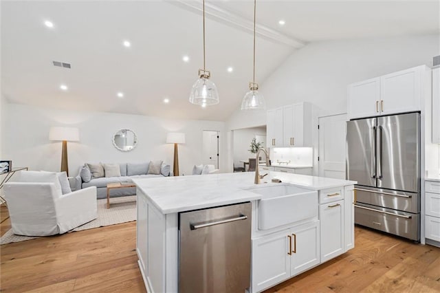 kitchen featuring white cabinets, appliances with stainless steel finishes, a kitchen island with sink, and beam ceiling