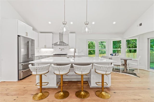 kitchen with white cabinetry, high quality fridge, a kitchen island with sink, and wall chimney range hood