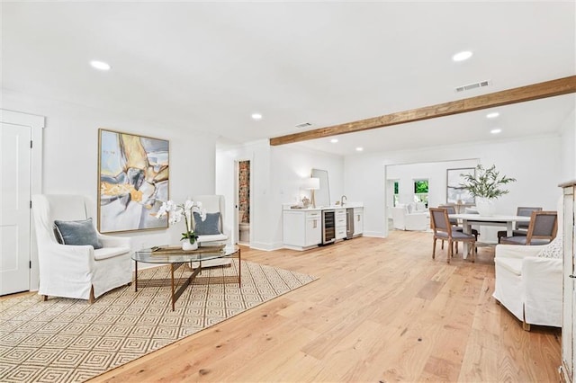 living area featuring beamed ceiling, light hardwood / wood-style flooring, and beverage cooler