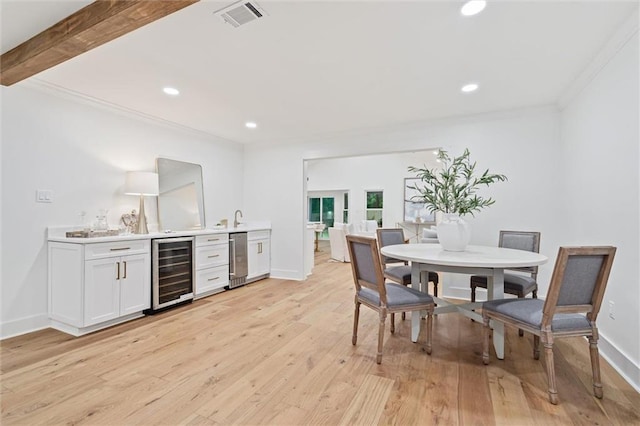 dining space featuring beamed ceiling, ornamental molding, beverage cooler, and light hardwood / wood-style flooring