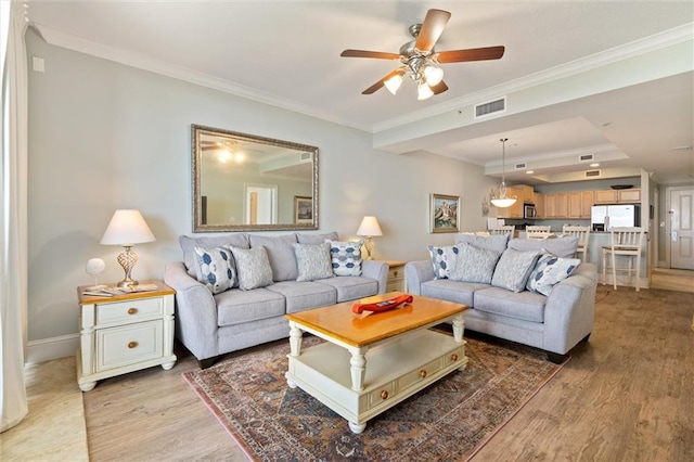 living area with ornamental molding, wood finished floors, visible vents, and baseboards