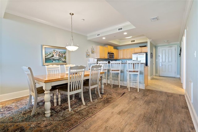 dining space featuring baseboards, visible vents, ornamental molding, wood finished floors, and a tray ceiling