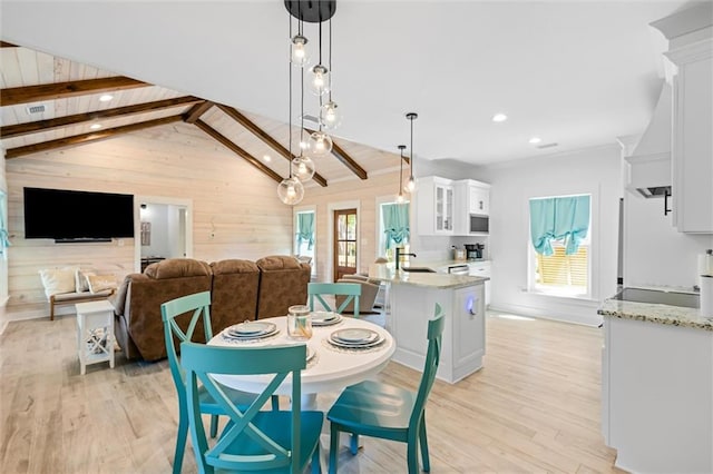 dining area featuring wood walls, vaulted ceiling with beams, light wood-type flooring, and sink