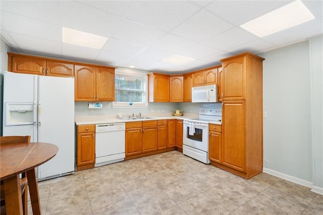 kitchen featuring light countertops, brown cabinetry, a sink, white appliances, and baseboards