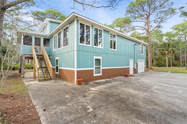 view of side of home featuring stairs, driveway, an attached garage, and a sunroom