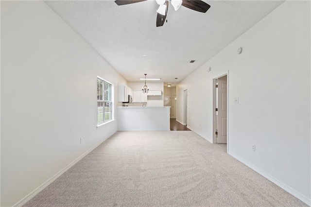 unfurnished living room featuring ceiling fan with notable chandelier and light colored carpet