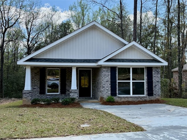 craftsman house with a front yard, a porch, brick siding, and a shingled roof