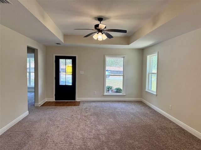 carpeted foyer entrance featuring a tray ceiling, visible vents, baseboards, and a ceiling fan