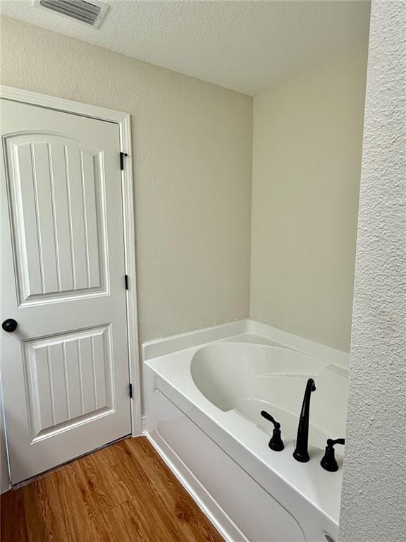 bathroom with a garden tub, visible vents, a textured ceiling, and wood finished floors