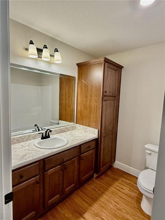 bathroom featuring toilet, wood finished floors, vanity, a textured ceiling, and baseboards