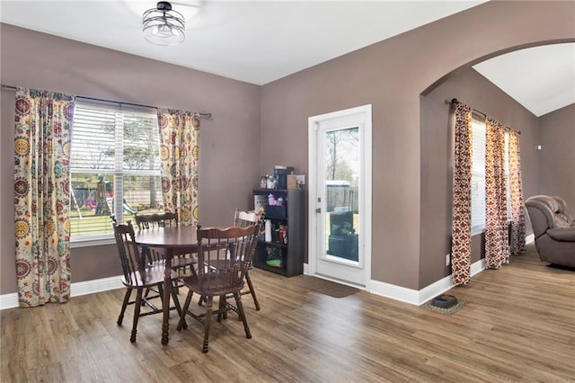 dining area with arched walkways, a wealth of natural light, and wood finished floors