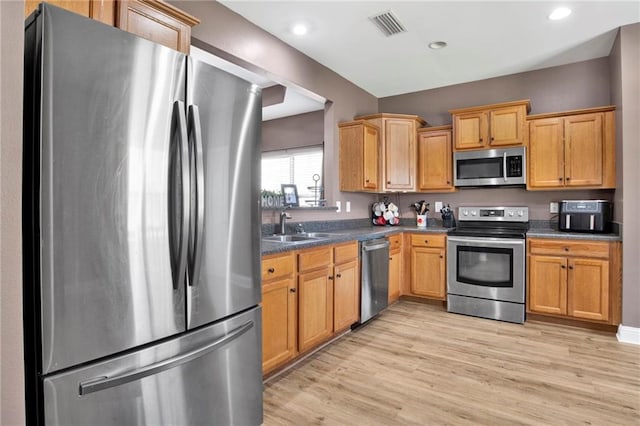 kitchen featuring visible vents, a sink, dark countertops, light wood-style floors, and appliances with stainless steel finishes