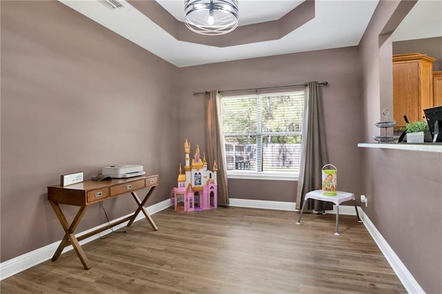 rec room with baseboards, a tray ceiling, and wood finished floors