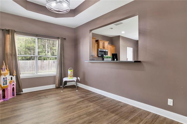 interior space featuring visible vents, a raised ceiling, baseboards, and wood finished floors